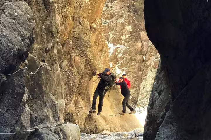 Two hikers navigating a narrow rocky cliff ledge using safety ropes in Fagaras Mountains