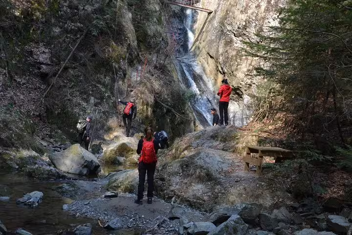 Hikers with red backpacks exploring a rocky gorge with waterfall on Fagaras hiking tour
