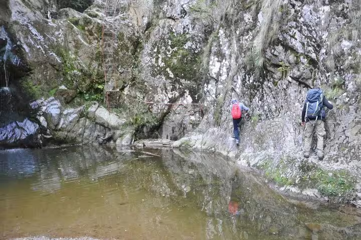 Two hikers climbing rocky gorge trail beside a tranquil mountain pool in Fagaras mountains, Romania