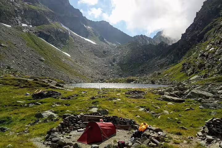 Red tent pitched beside alpine lake in Fagaras Mountains rocky cirque with snow patches above