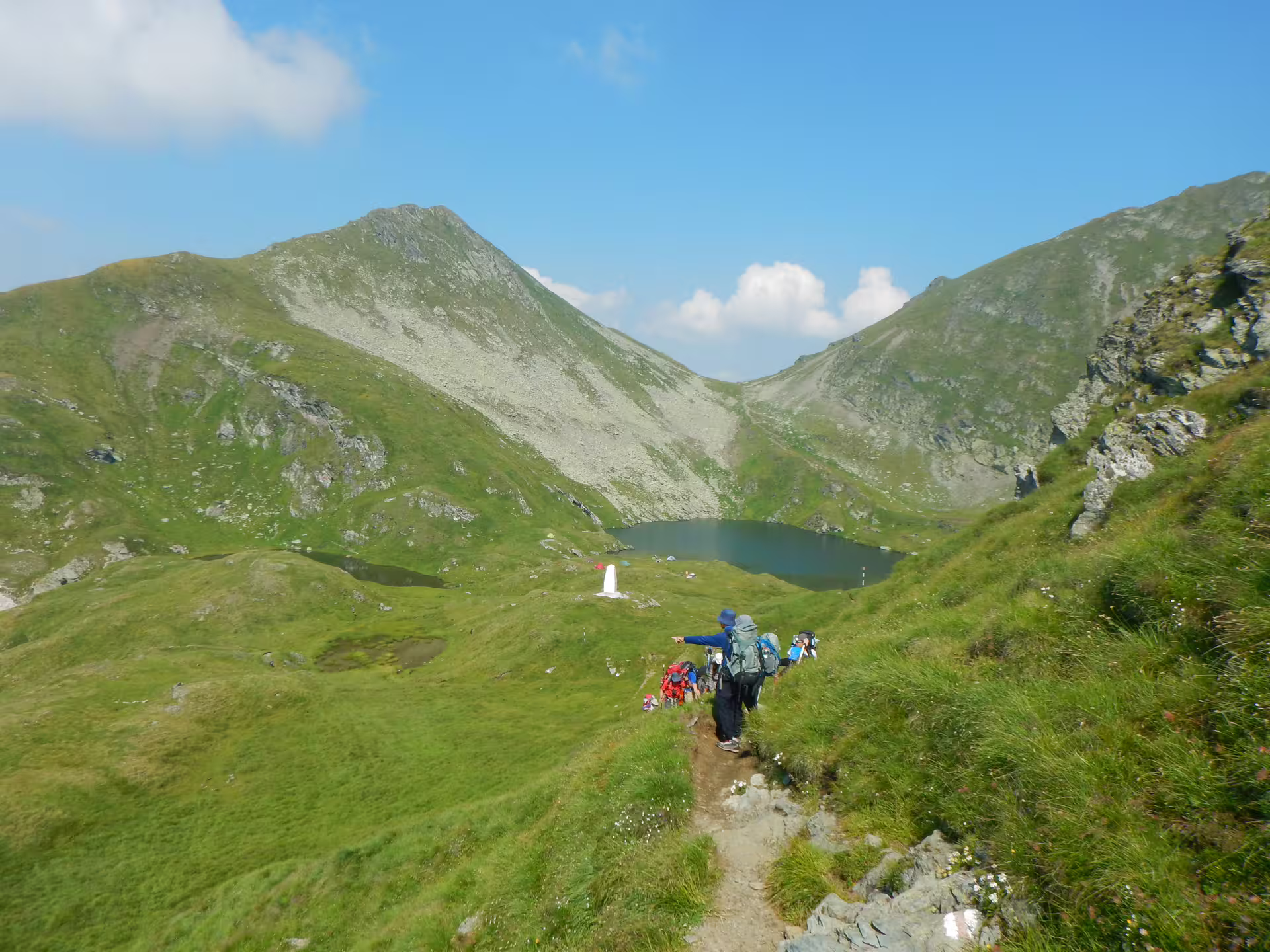 Hikers trekking down mountain trail toward alpine lake in Fagaras Mountains, Romania