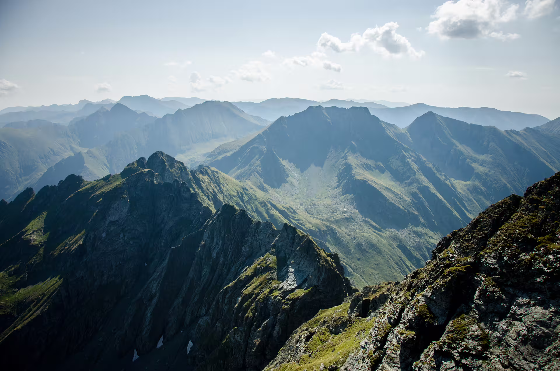Panoramic view of Fagaras Mountains ridgelines and green valleys from a rocky summit in Romania