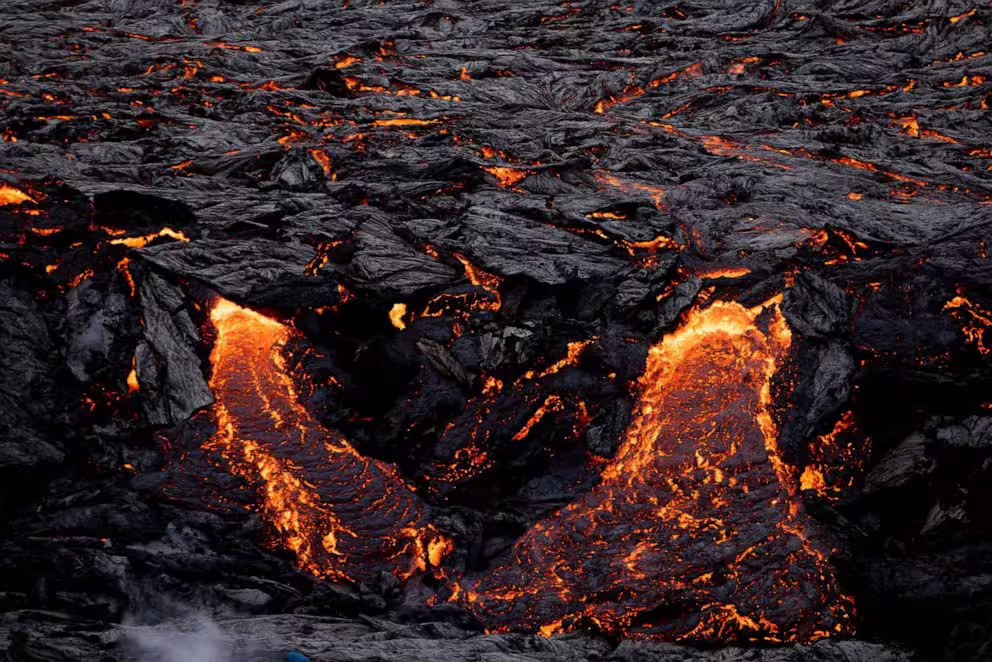 Glowing orange lava flows breaking through dark hardened volcanic rock at Fagradalsfjall volcano Iceland