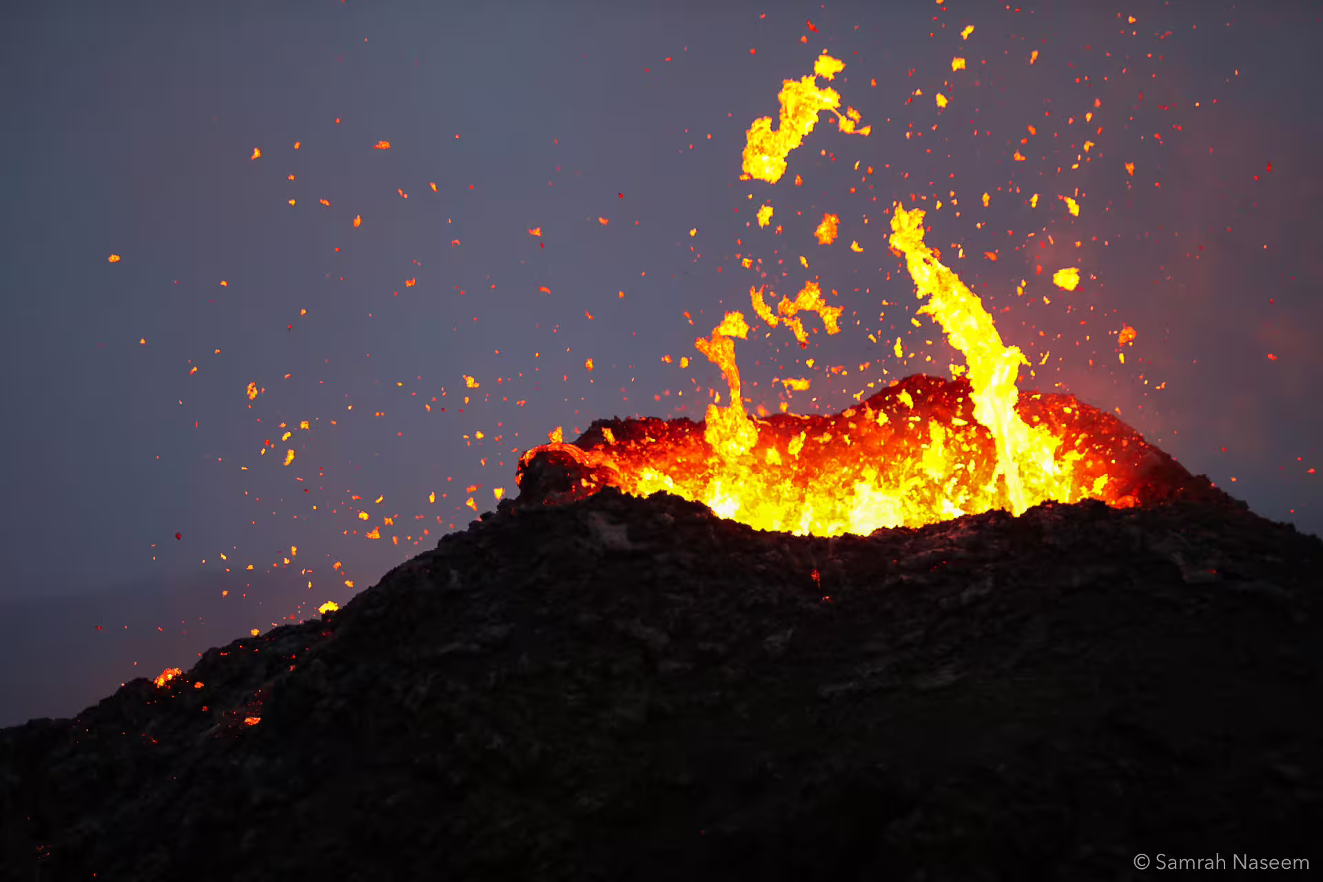 Lava erupting from Fagradalsfjall volcano crater at dusk with glowing lava fountains and sparks