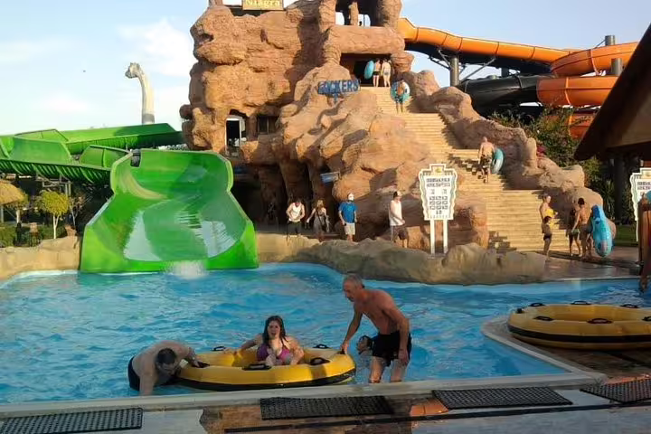 Families floating in a wave pool near green slide and rock tower at Sharm El Sheikh aqua park day pass