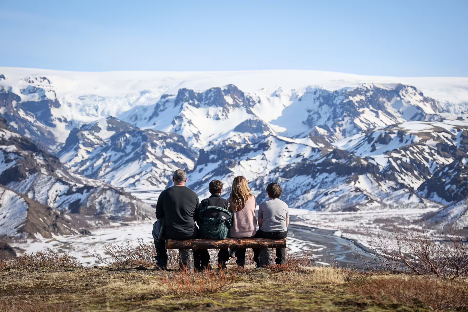 A family sits on a bench admiring the breathtaking snow-covered Thorsmork mountain landscape on a full-day Iceland 4x4 tour.