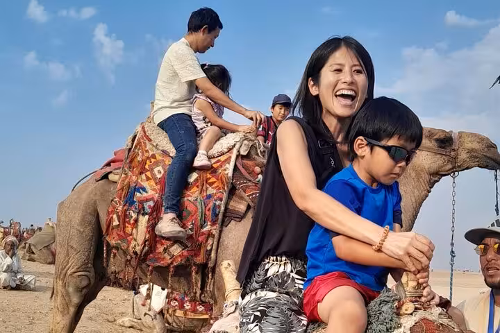 Family camel ride at Giza Pyramids plateau on a Cairo private tour, desert view and local guide nearby