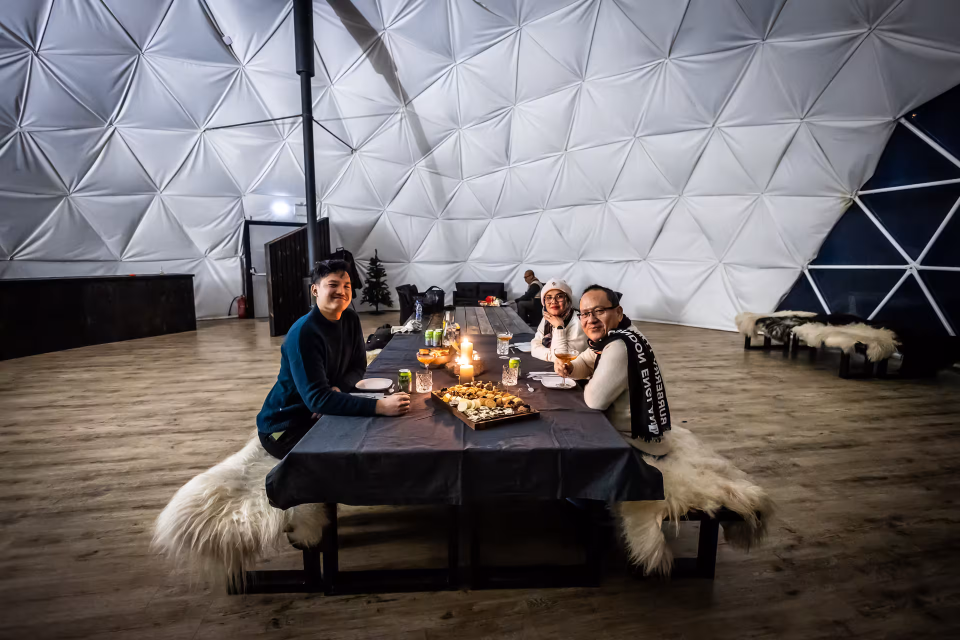 Family enjoying a cozy candlelit dinner inside a geodesic dome during a northern lights Iceland tour experience