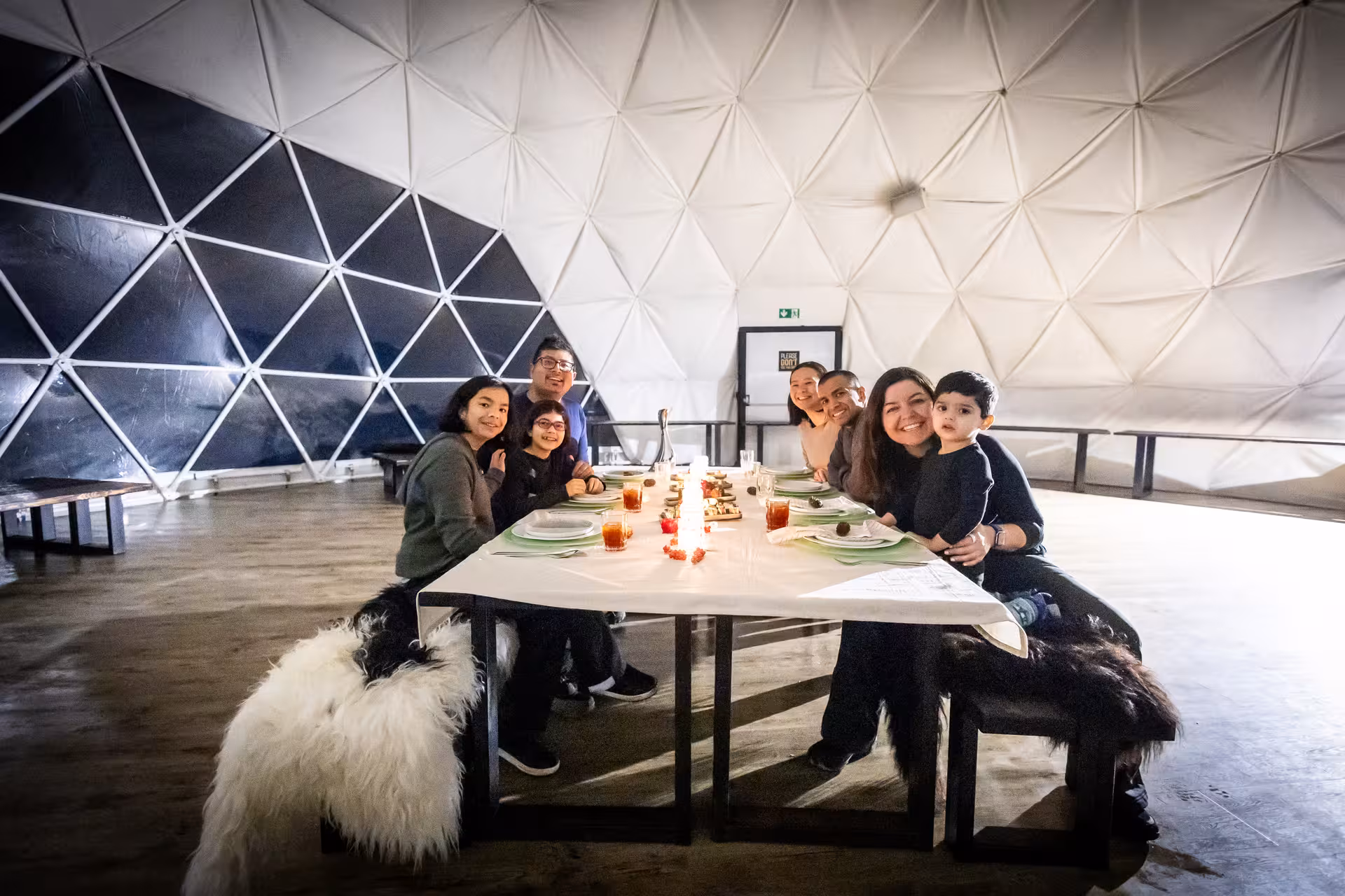 Family enjoying candlelit dinner under northern lights in cozy Iceland geodesic dome experience