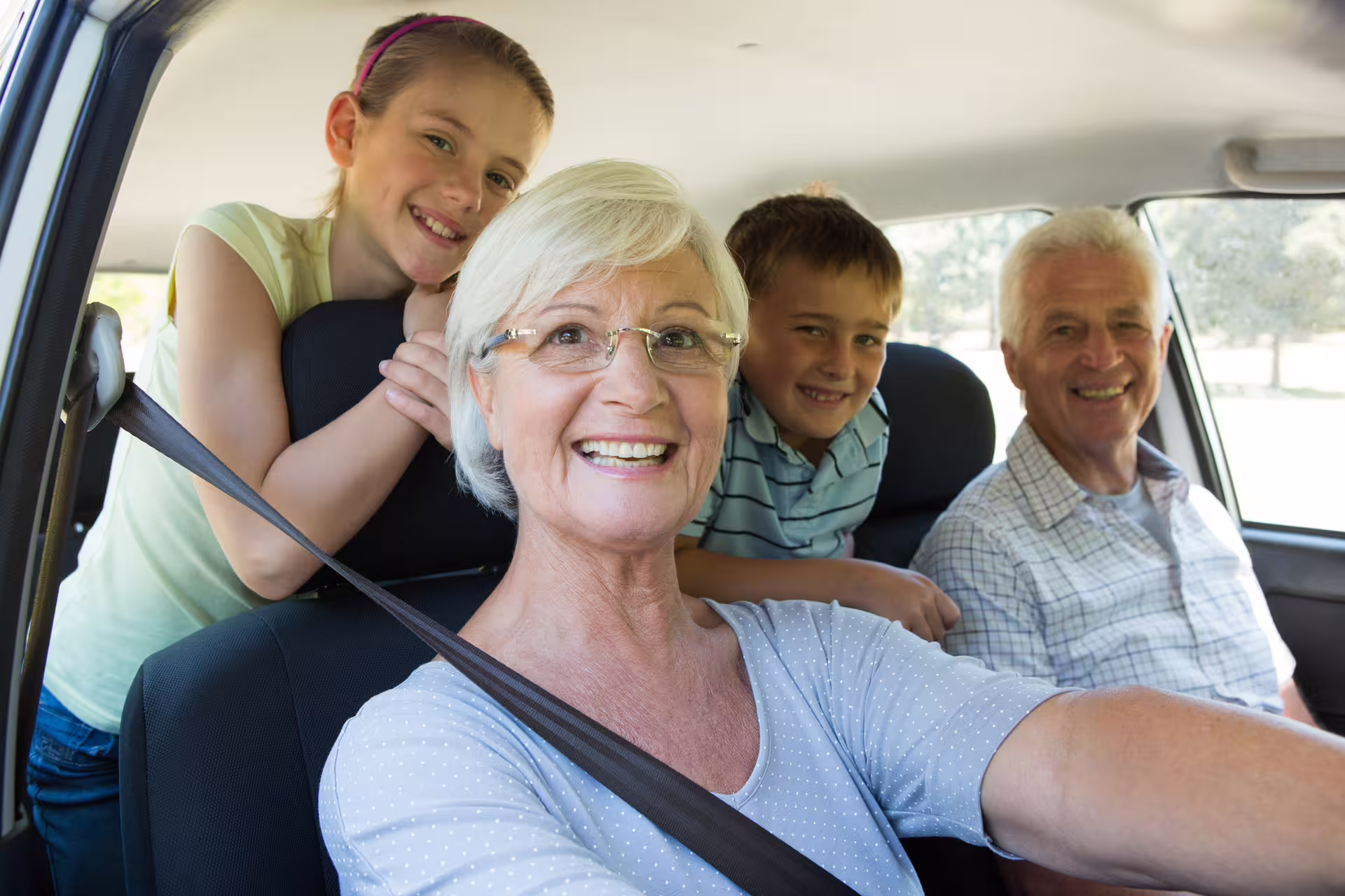 Grandparents and grandchildren smiling together inside a car ready for a transfer trip