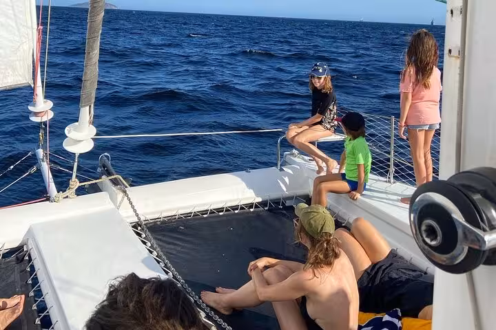 Family lounging on catamaran nets over Rio waters on a private 3-hour Velas do Rio sailboat tour open bar