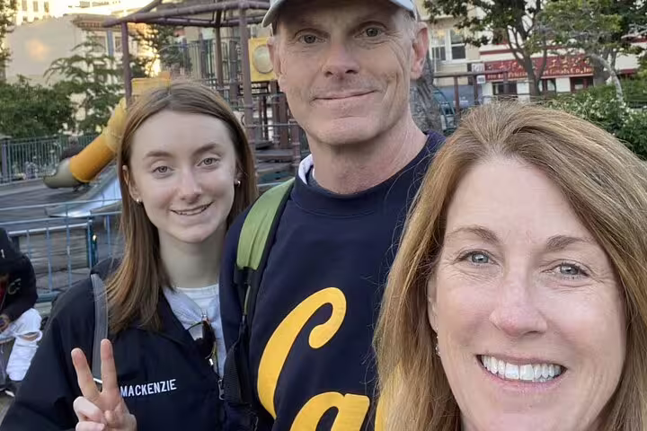 Family of three smiling at a San Francisco park with playground equipment in background