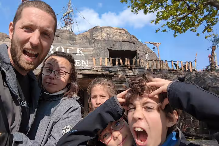 Family taking a fun selfie at the Wurstelprater amusement park in Vienna with a rocky pirate-themed attraction behind them