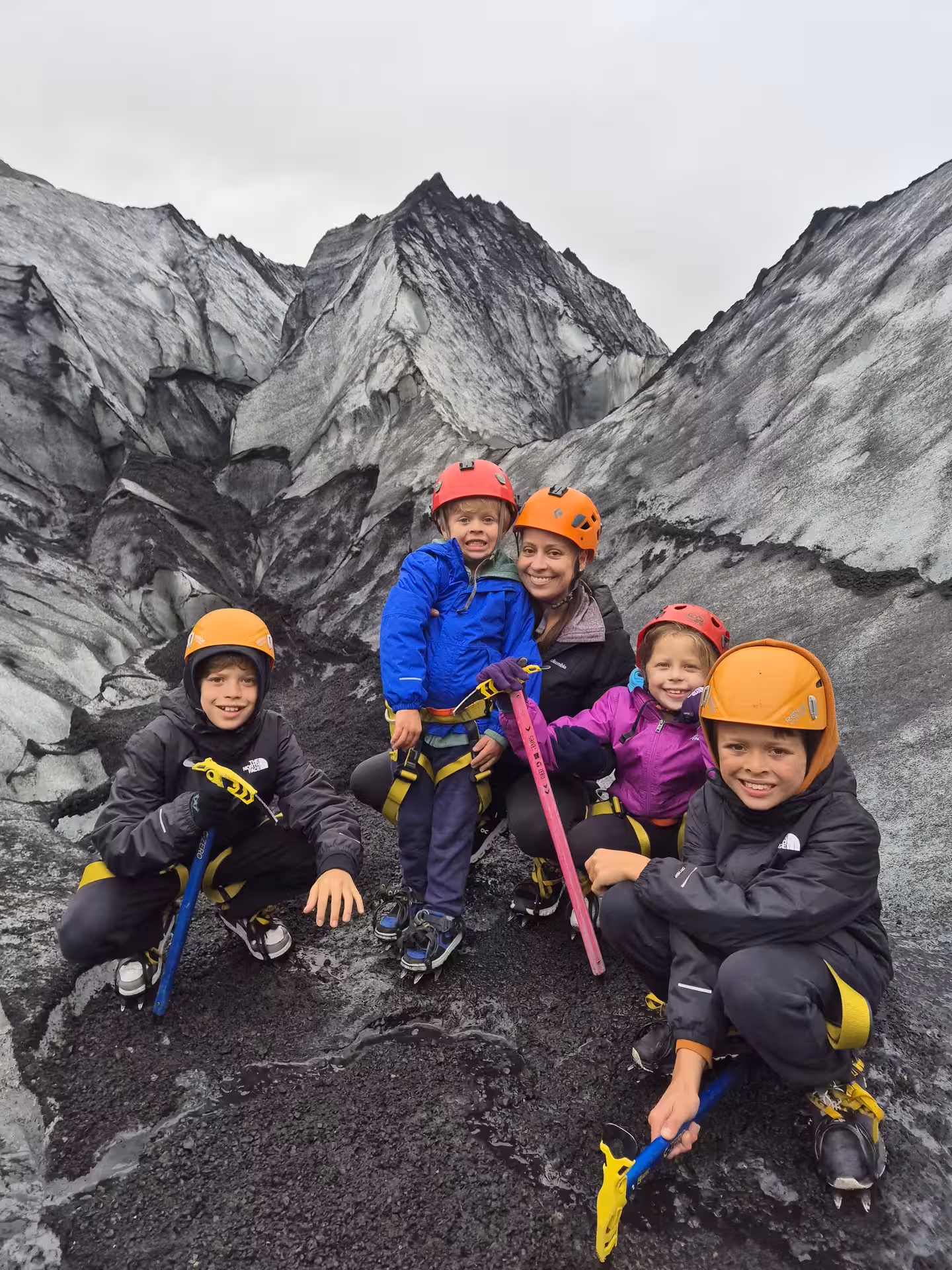 Family with helmets and crampons posing on Iceland glacier with volcanic ice formations behind
