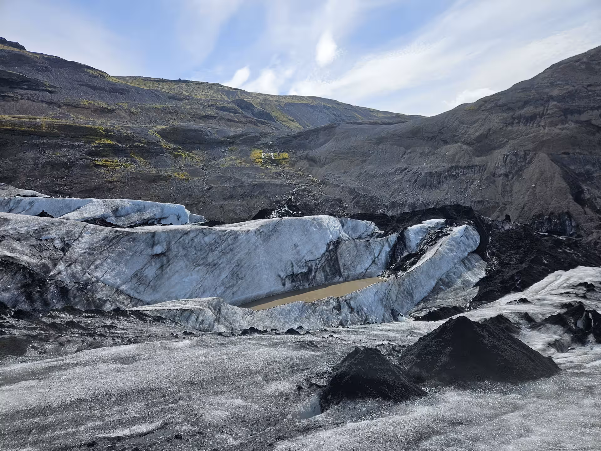 Black volcanic ash-covered glacier with blue ice formations and rocky mountain valley in Iceland