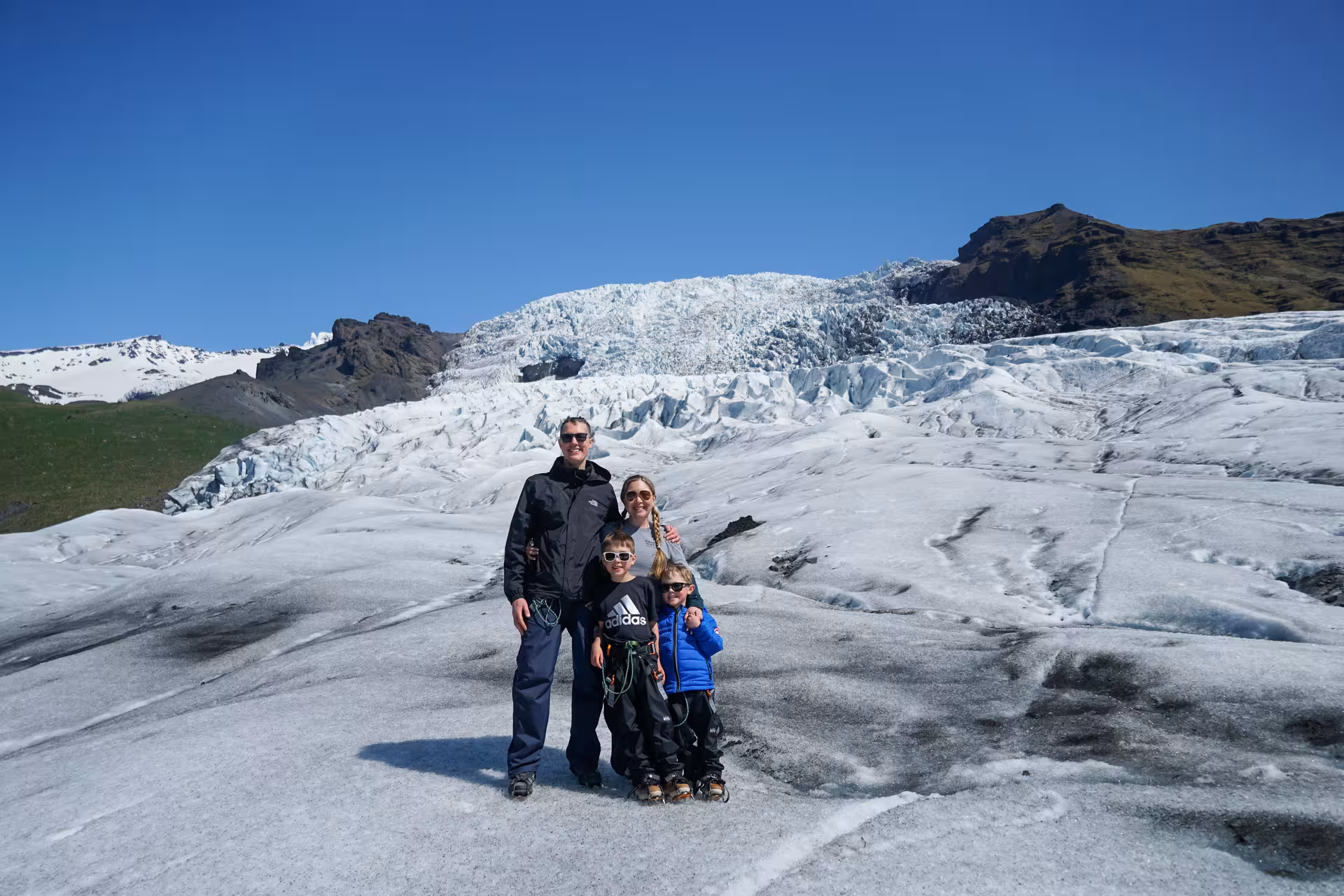 Family posing on Iceland glacier during a full-day guided glacier hike tour under a clear blue sky