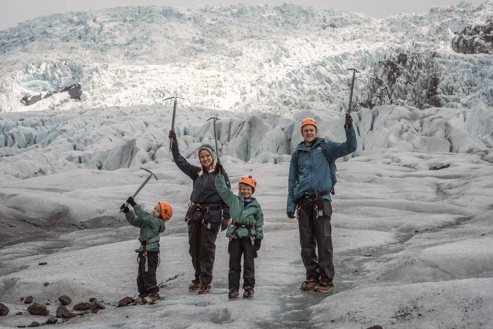 Family with ice axes and helmets posing on Iceland glacier during a full-day guided glacier hiking tour