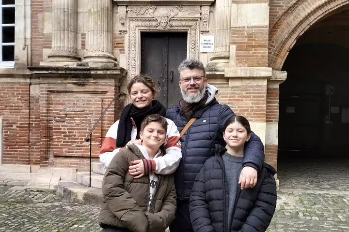 Family of four smiling in front of a historic brick building in Toulouse, France