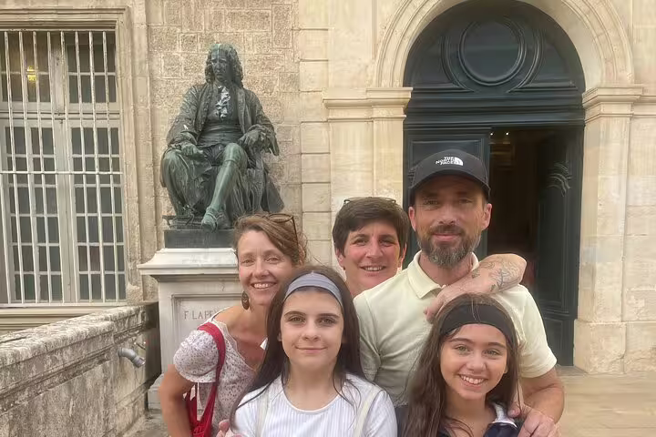 Family of five posing in front of a bronze statue at a historic stone building in Montpellier