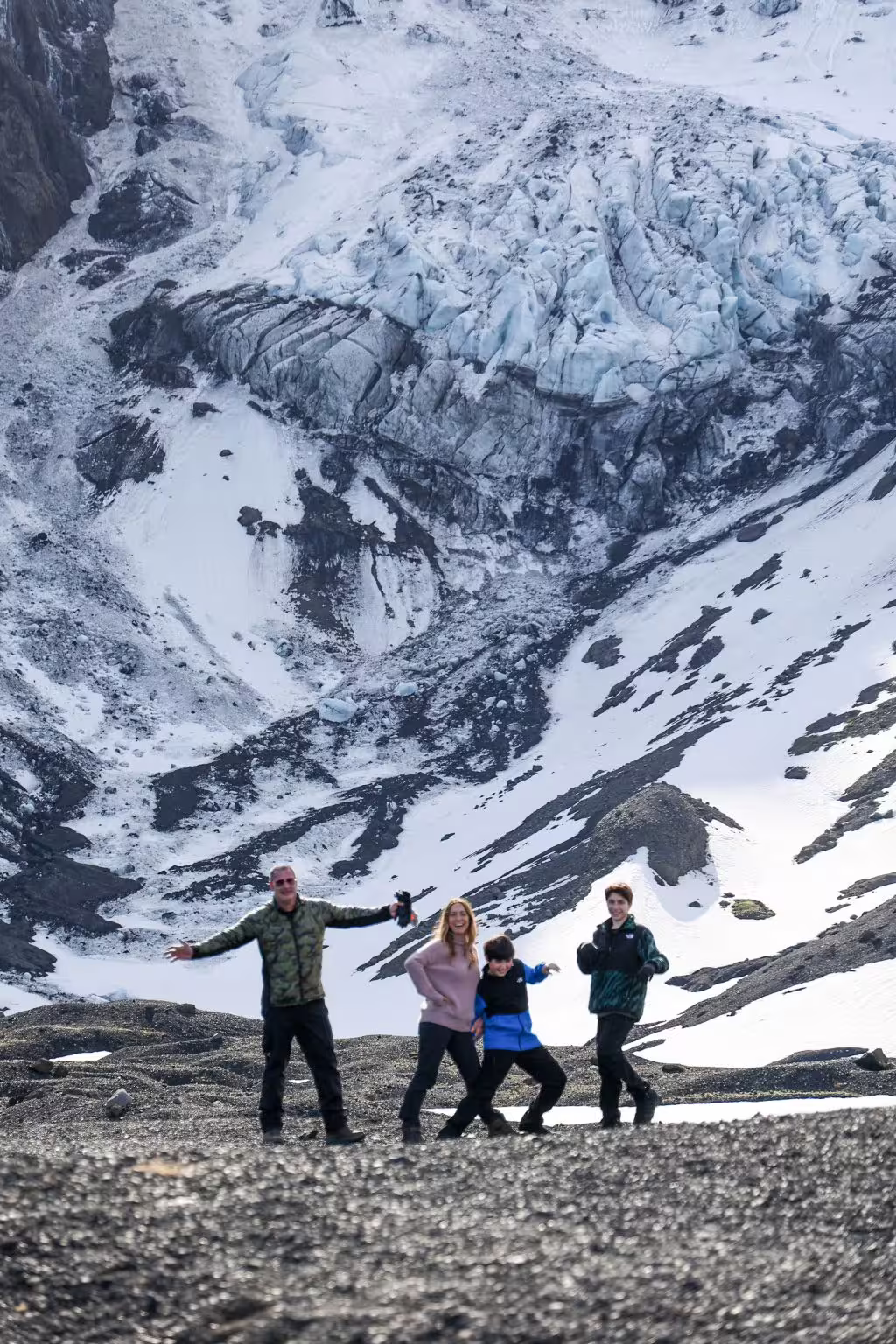 Happy family posing on rocky highland terrain with a dramatic snow-covered glacier and mountain backdrop