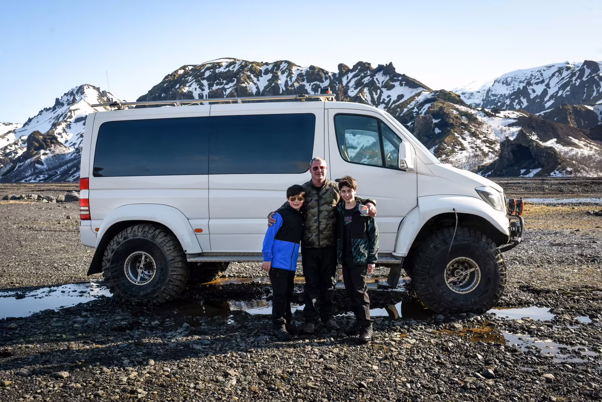 Family posing with a 4x4 super jeep van amid snow-capped Iceland highlands on a 12-day grand tour adventure