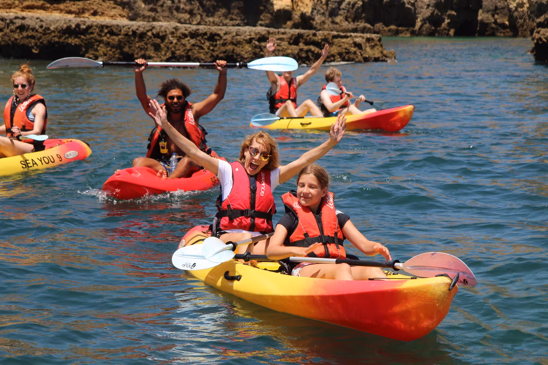 Happy family group kayaking on clear blue water near Lagos Algarve cliffs during a guided sea cave adventure tour