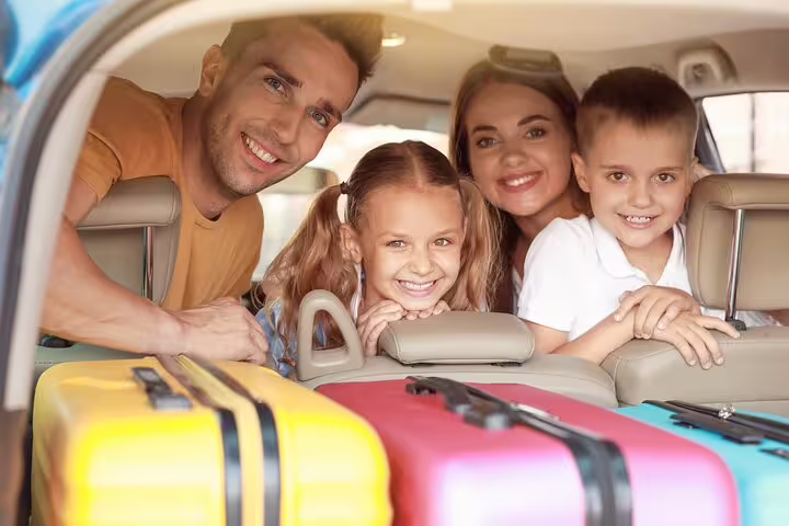 Happy family with colorful luggage in car trunk ready for airport transfer