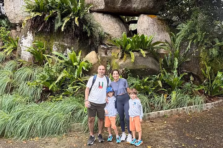 Family enjoying a picturesque moment in front of lush vegetation and unique rock formations on Mahe Island tour.