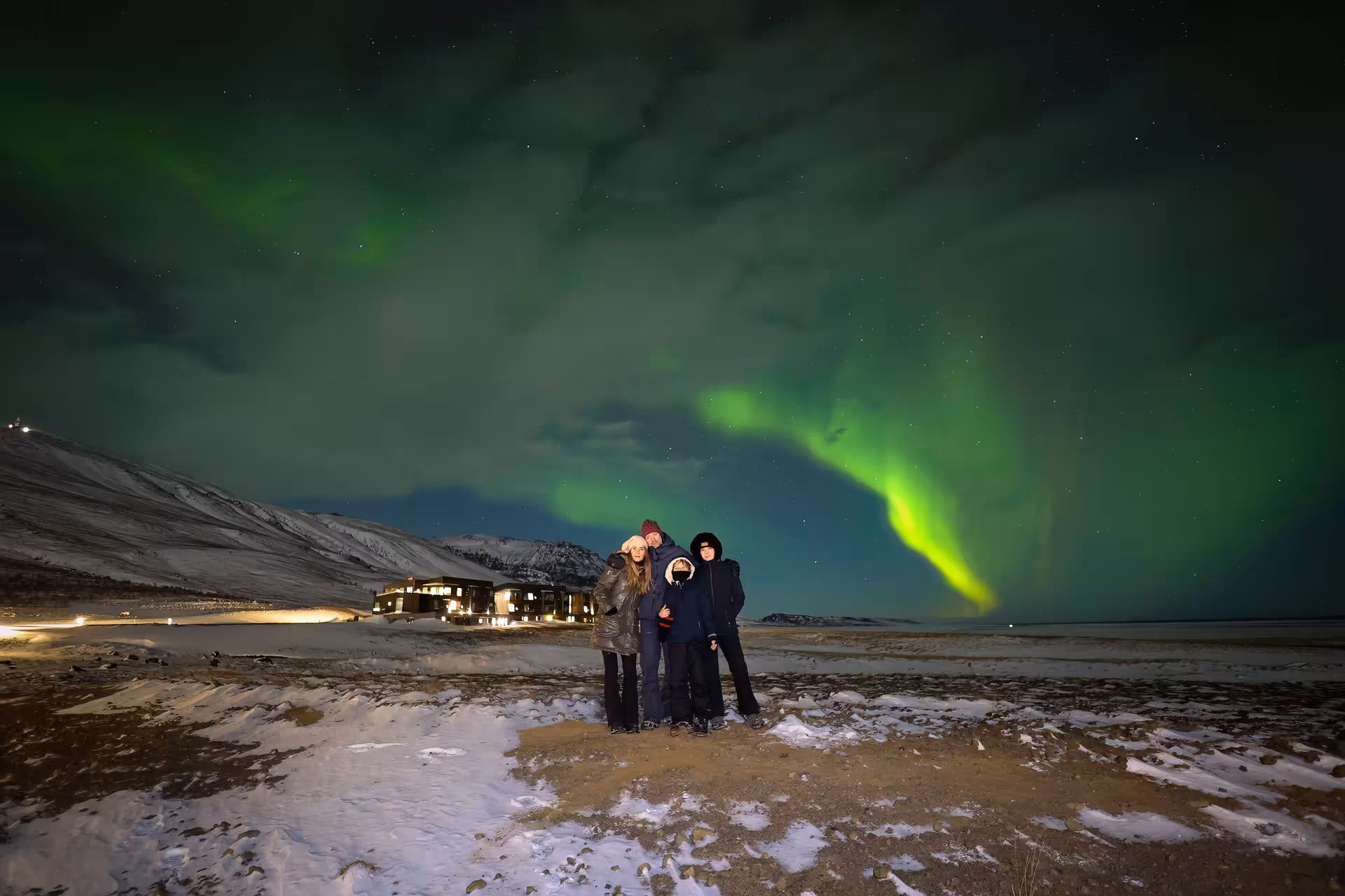Family posing together under spectacular green northern lights aurora display on a snowy Iceland winter night.