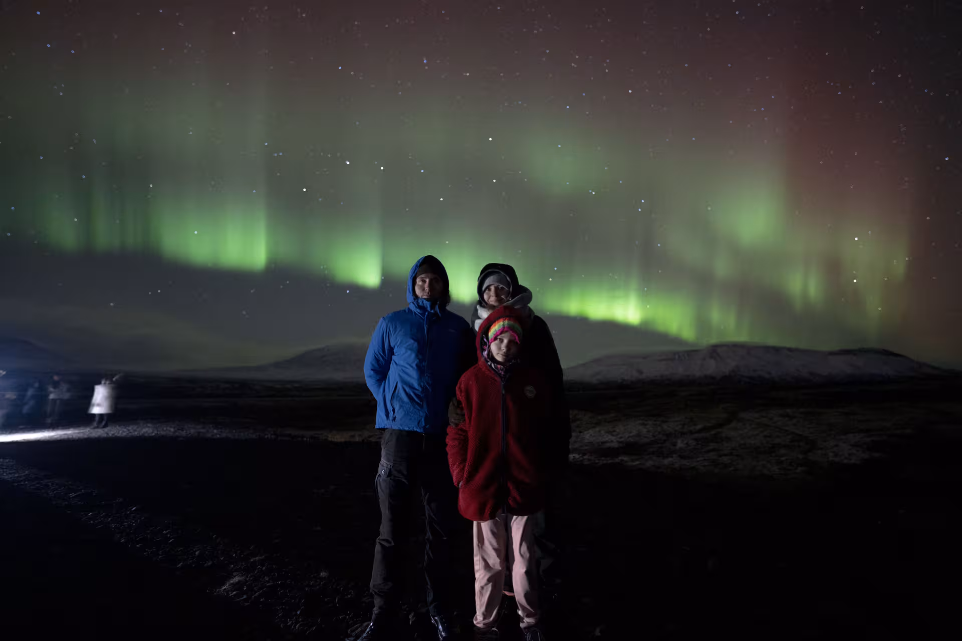 Family posing under vivid green and red northern lights on a guided night tour near Reykjavik