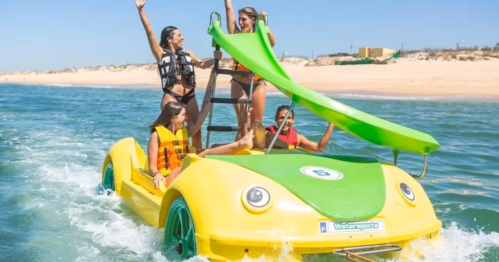 Family enjoying a fun pedal boat tour with a green slide on sparkling ocean waters near a sunny beach.