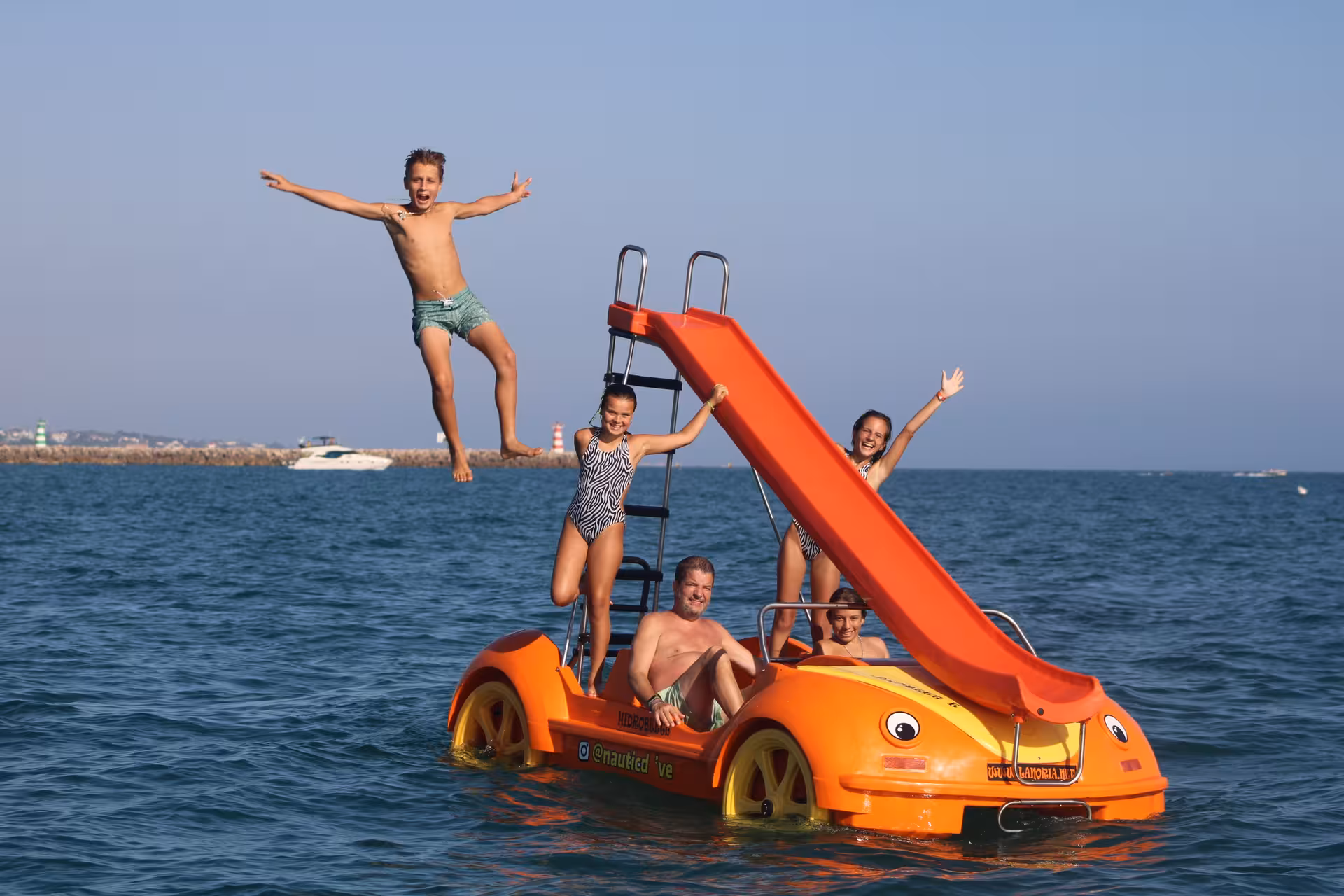 Kids and family enjoying a fun pedal boat tour with a water slide on the open sea on a sunny day.