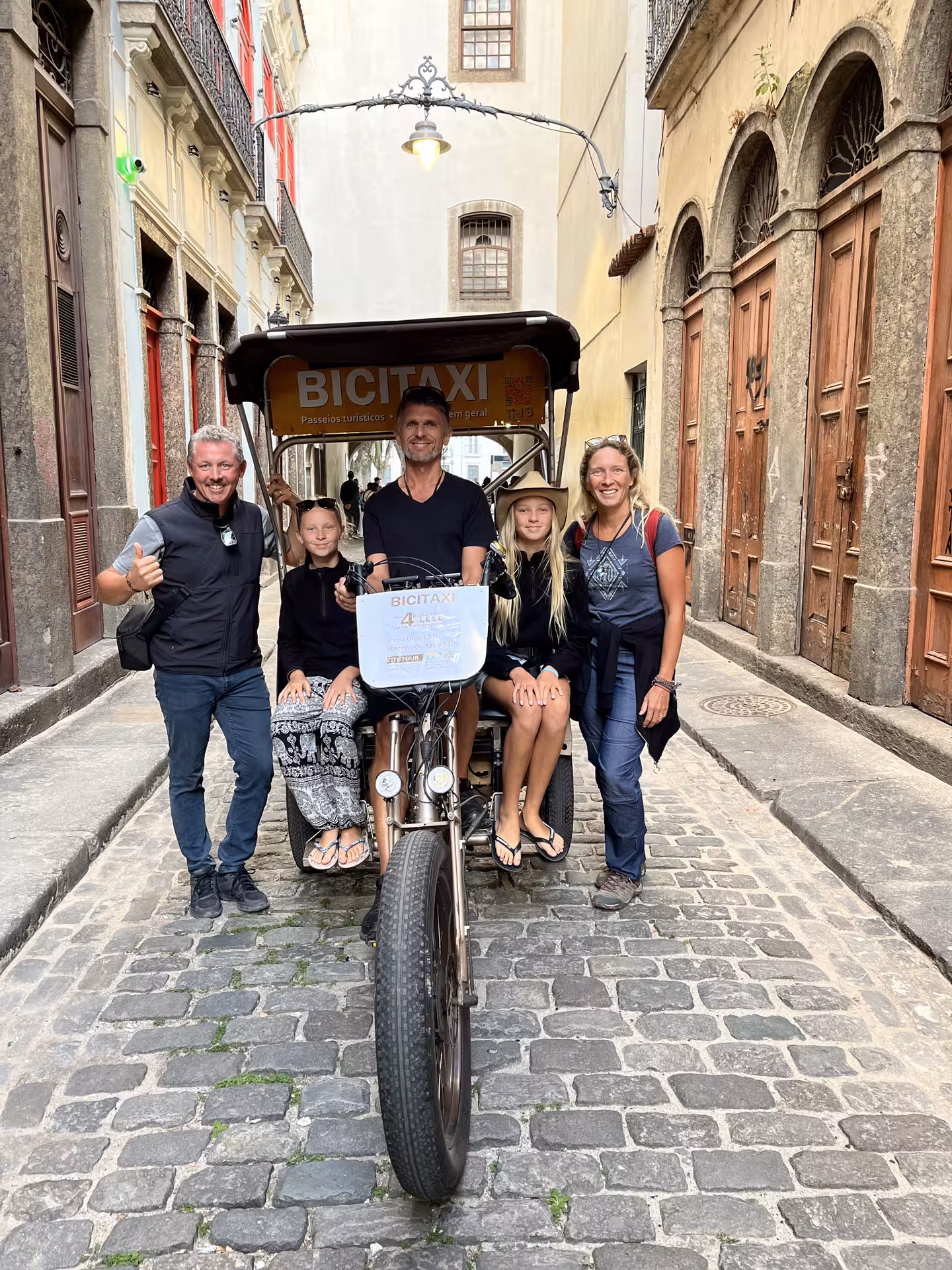 Family poses with bicitaxi pedicab on Rio de Janeiro historic city centre tour along cobblestone lane