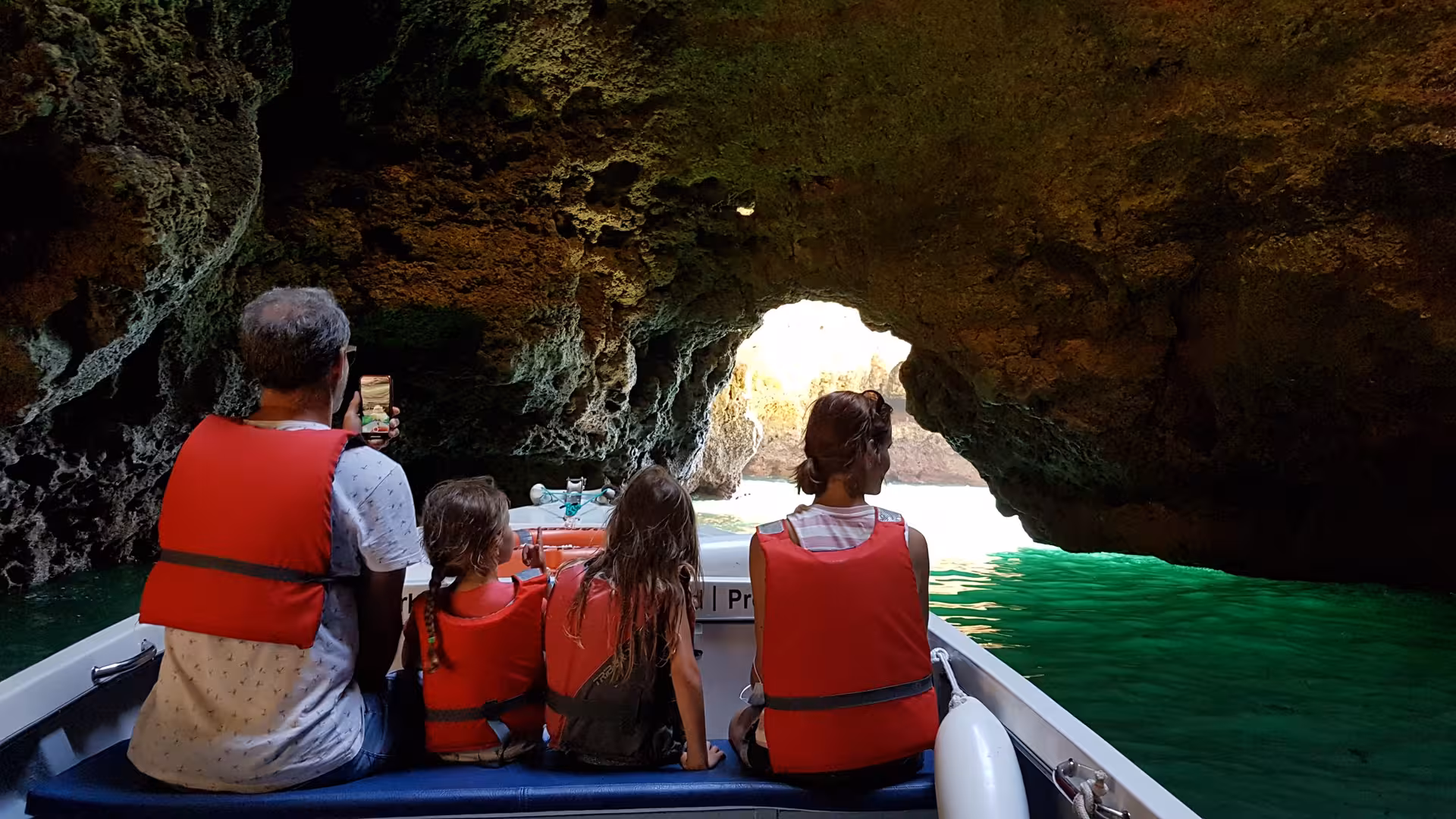 Family in life jackets on a Lagos grotto boat tour gliding through Ponta da Piedade cave toward bright turquoise water