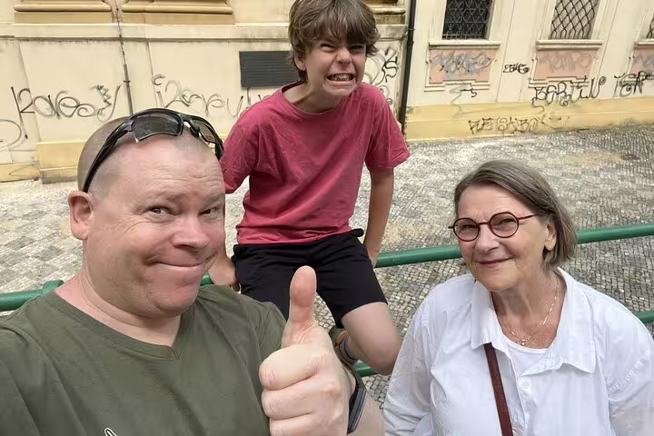 Family of three smiling during Prague Old Town self-guided walk, graffiti-covered historic building behind them