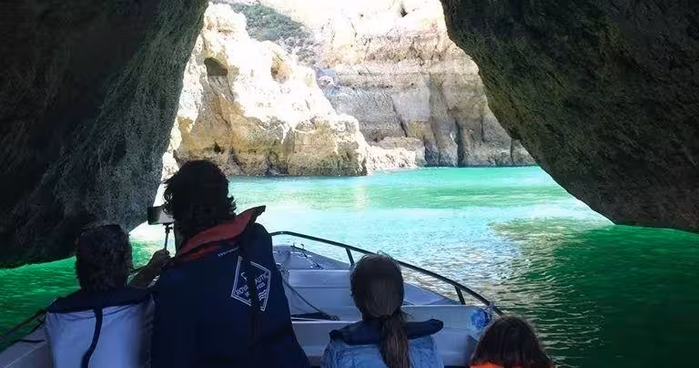 Family on private Algarve boat tour cruising through coastal caves toward bright turquoise water and towering limestone cliffs