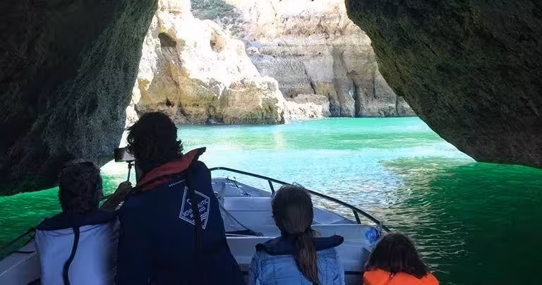 Family enjoying a private 2-hour Algarve cave tour by boat, entering a rocky grotto with crystal-clear emerald green sea