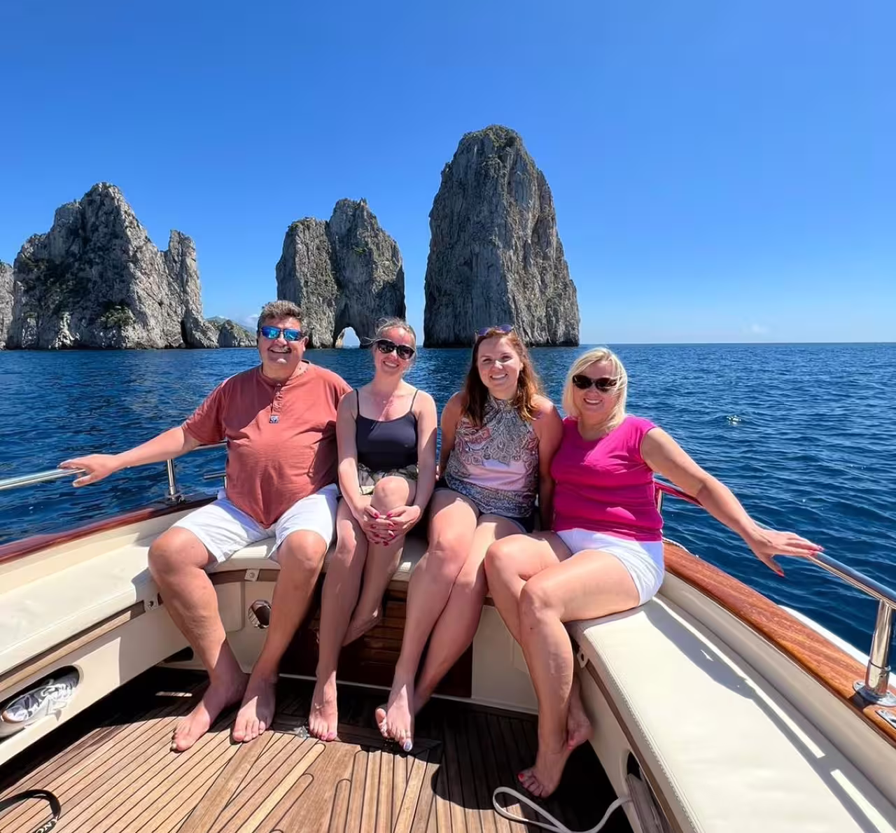Family relaxing on a private boat tour with Capri's stunning Faraglioni rocks in the background.