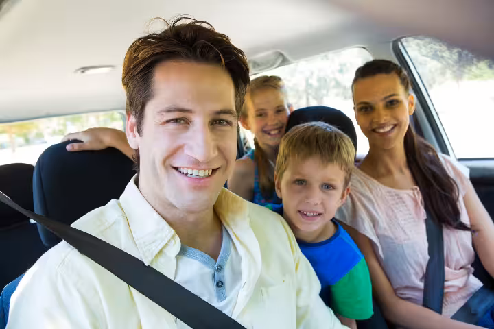 Family of four smiling inside a private sedan car during airport transfer