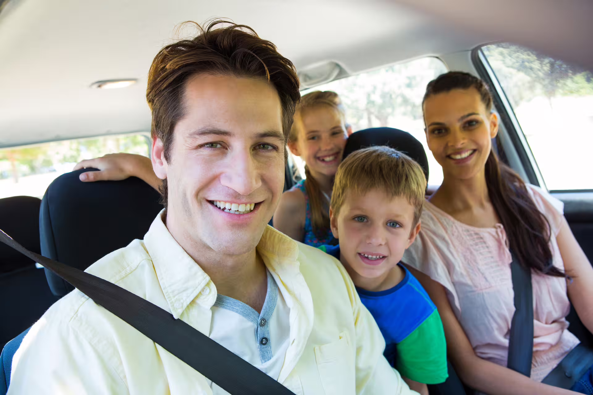 Family of four smiling inside a private sedan car with seatbelts fastened