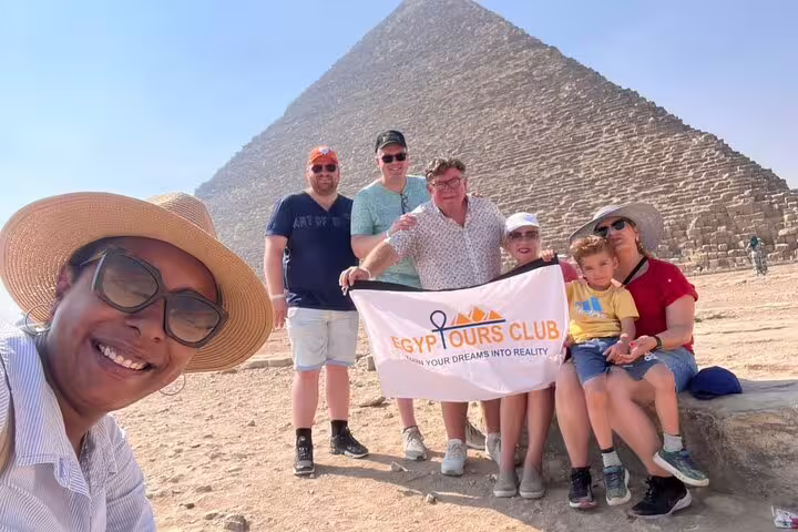 Family group photo at Great Pyramid of Giza with tour guide banner, private Giza pyramids and Egyptian Museum tour
