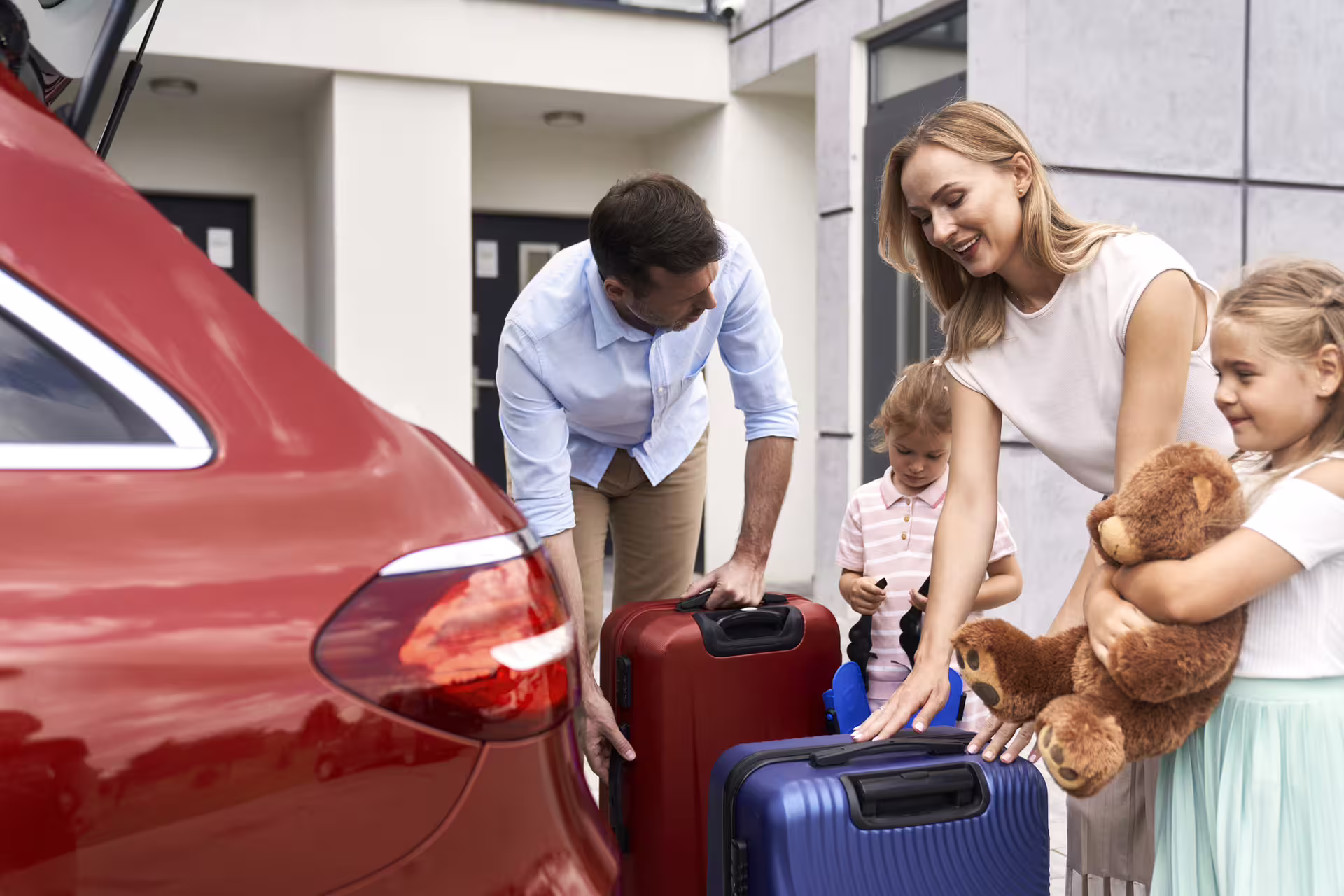 Family loading red and blue suitcases into car trunk for private transfer trip
