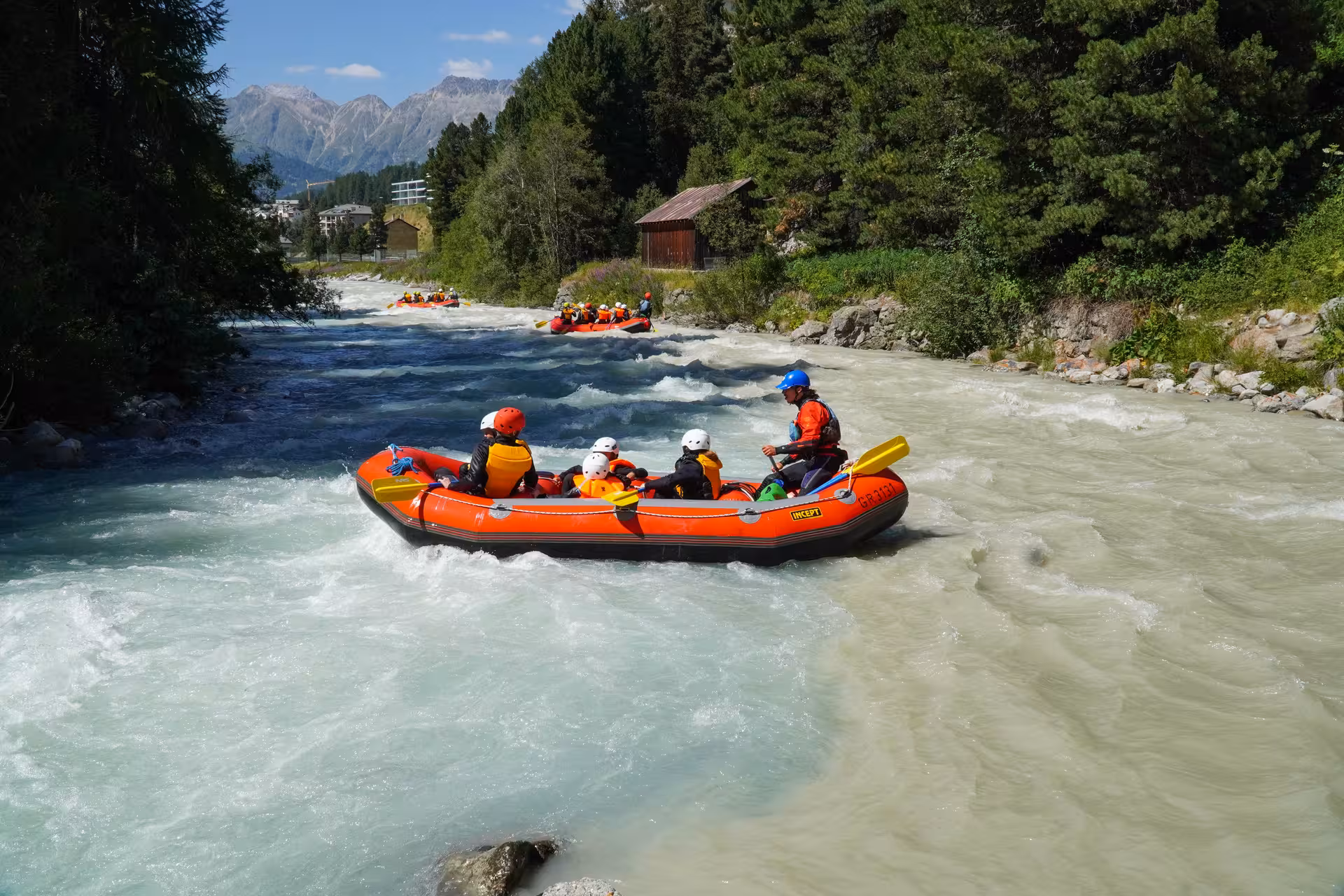 Group rafting through lively rapids in Engadin, surrounded by stunning alpine scenery and clear blue skies.