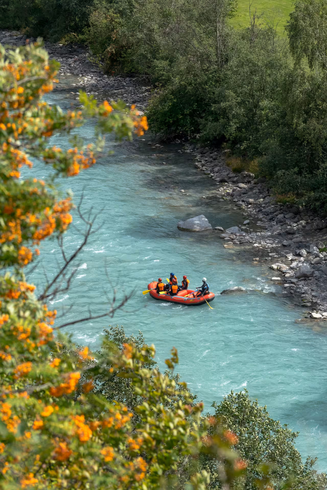Family enjoying rafting on the scenic turquoise river in Engadin, surrounded by lush greenery and vibrant flowers.
