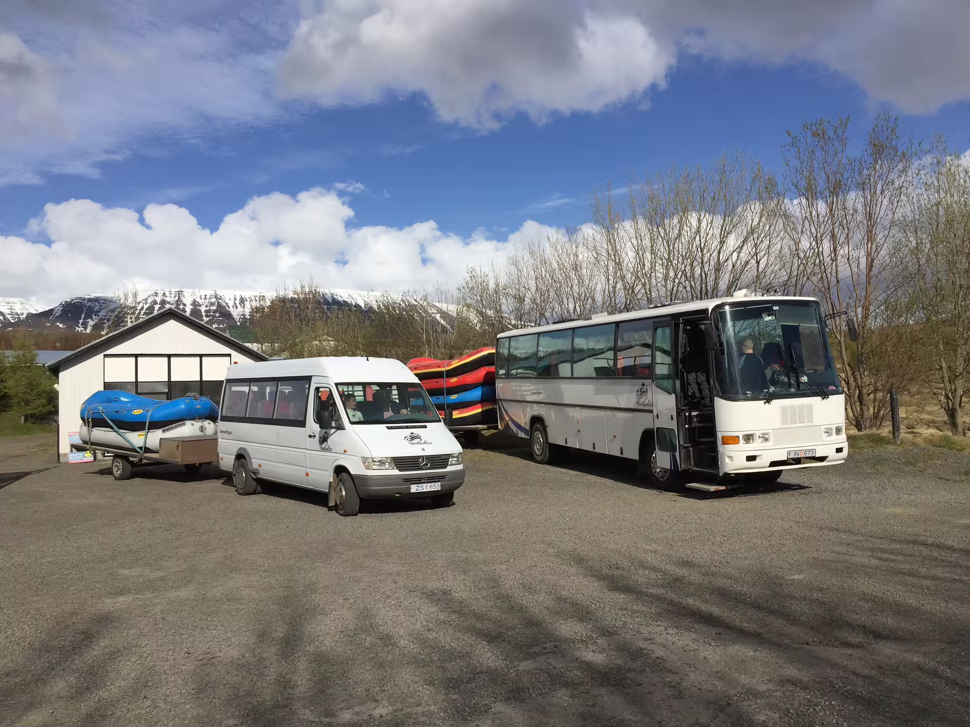 Buses and vans ready for a family river rafting adventure, with rafts loaded, set against a scenic mountain backdrop.