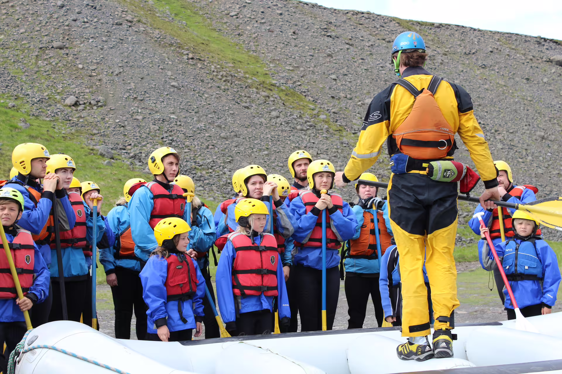 Instructor briefing a group of families in safety gear before an exciting river rafting adventure in scenic outdoor setting.