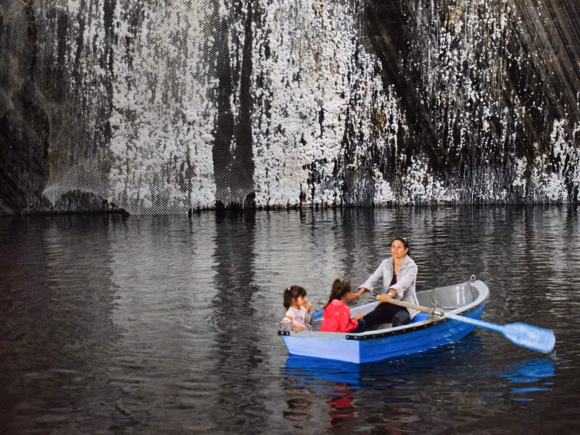 Family rowing a blue boat on the underground lake inside Turda Salt Mine during a guided tour from Cluj Romania