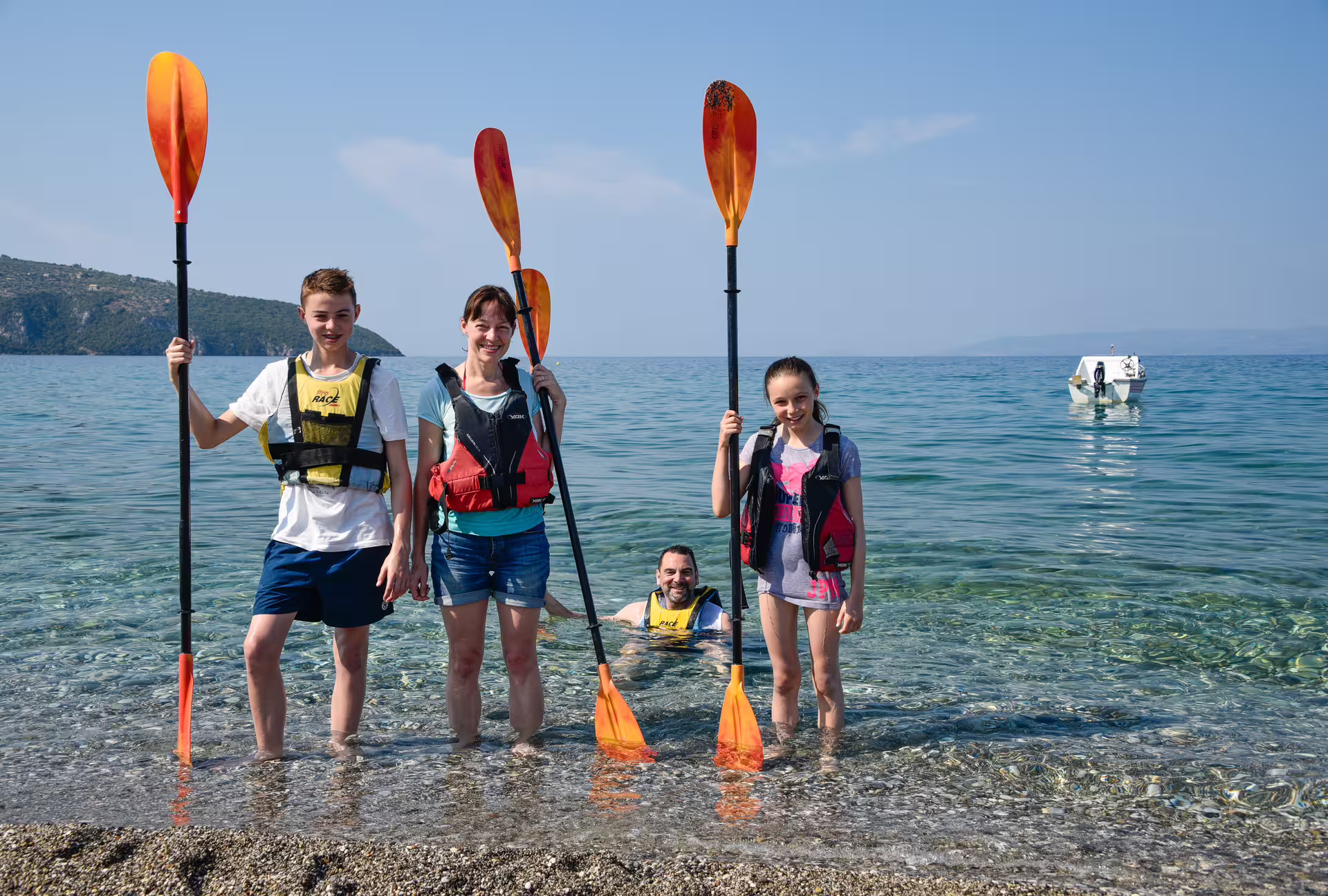 Family ready for sea kayak tour in Kalamata, Greece, holding paddles on a crystal-clear beach in Messinia