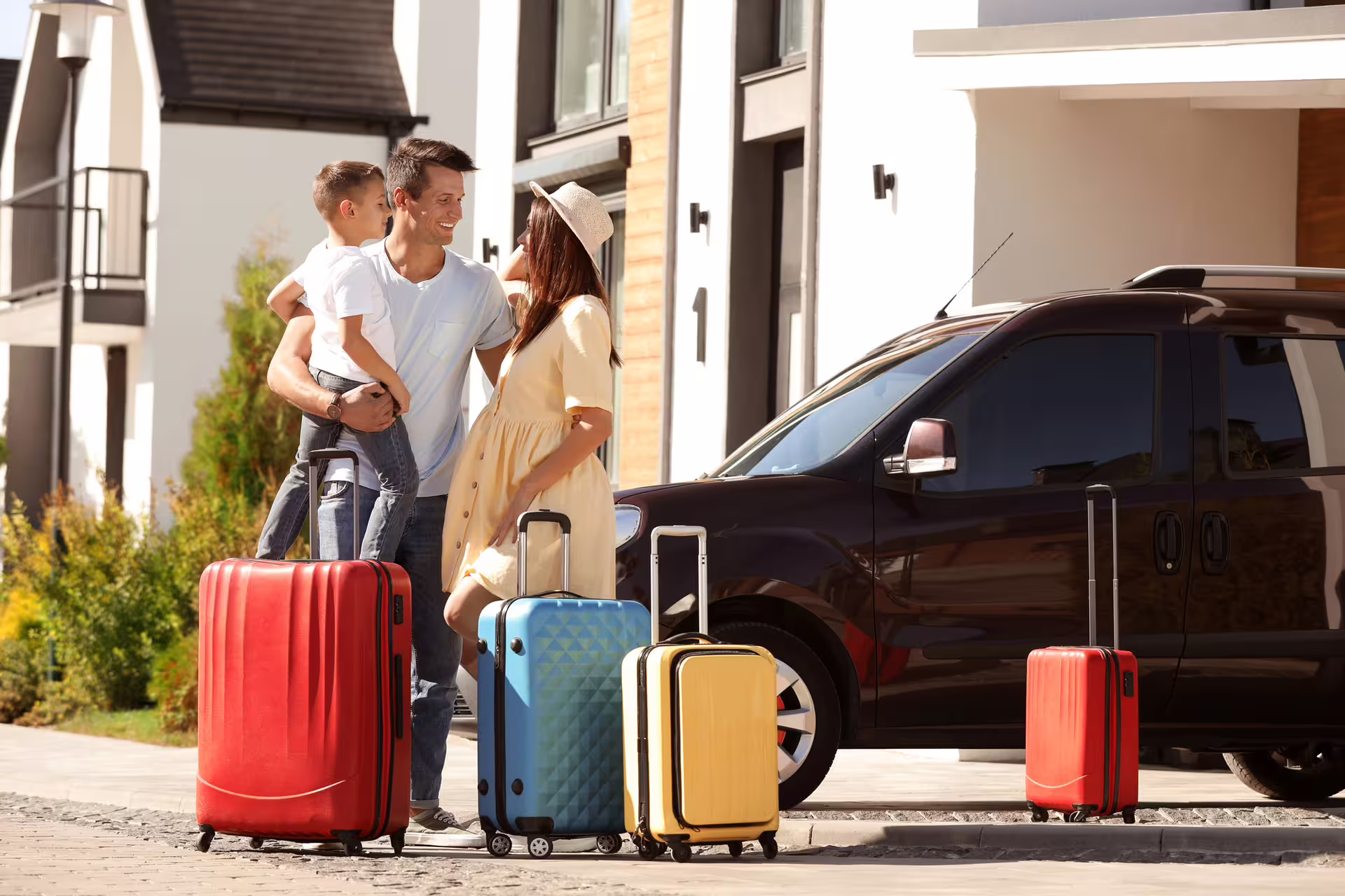 Family with colorful luggage loading a dark sedan for airport transfer