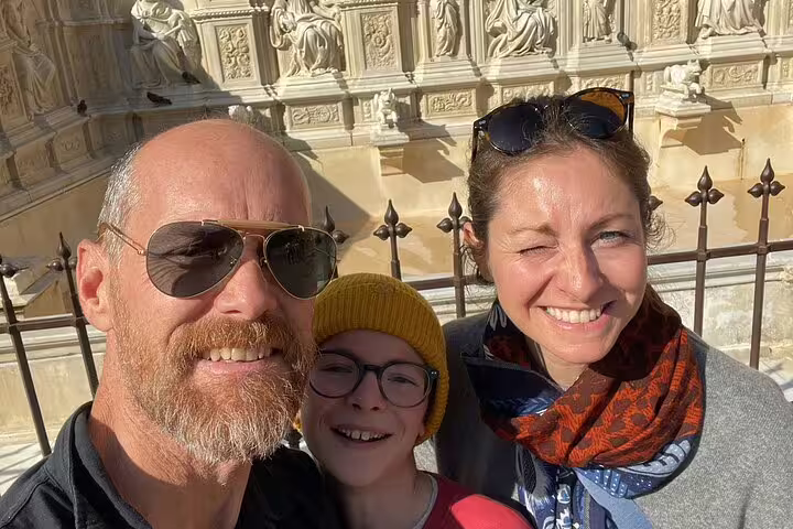 Family of three smiling in front of ornate medieval cathedral facade in Siena, Italy